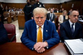 Donald Trump seated in a courtroom with a serious expression, surrounded by legal representatives and court officials.