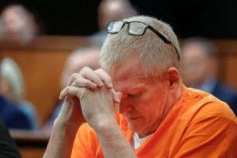 Alex Murdaugh, wearing an orange prison jumpsuit, sits with his hands clasped and head bowed during a court proceeding.
