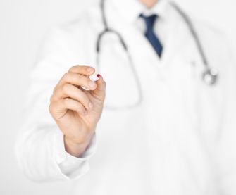 A medical professional in a white coat holding a pen, suggesting a professional context.
