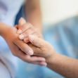 A caregiver holding the hand of an elderly person in a nursing home setting. A caregiver holding the hand of an elderly person in a nursing home setting.