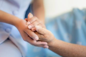A caregiver holding the hand of an elderly person in a nursing home setting.