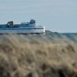 A ferry on the water near a shoreline, with grass in the foreground. A ferry on the water near a shoreline, with grass in the foreground.