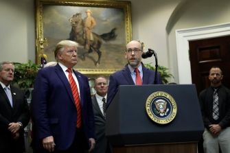 A press conference featuring government officials, including a speaker at a podium with the presidential seal, discussing matters related to federal employee layoffs during a government shutdown.