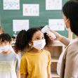 A teacher checking the temperature of a student in a classroom while other students wait in line, all wearing masks. A teacher checking the temperature of a student in a classroom while other students wait in line, all wearing masks.