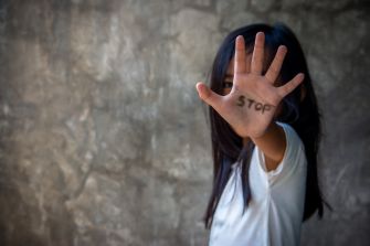 A child holds out their hand with the word "STOP" written on it, symbolizing a call to end forced labor and human trafficking.