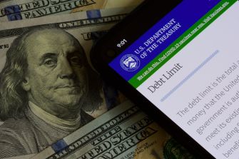 Image of a smartphone displaying information from the U.S. Department of the Treasury about the debt limit, with a backdrop of U.S. currency featuring Benjamin Franklin.