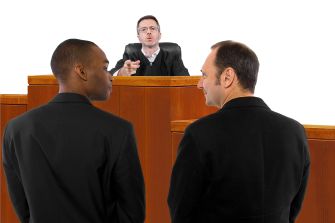 Two men in formal attire standing in a courtroom facing a judge.