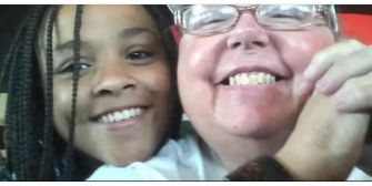 A smiling woman and a girl with braided hair, embracing and posing for a photo together.