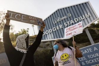 Protesters holding signs outside Dodger Stadium advocating against ICE presence and expressing anti-Trump sentiments.