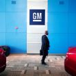 A person walking past General Motors branding in a showroom with red cars in view. A person walking past General Motors branding in a showroom with red cars in view.