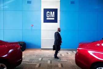 A person walking past General Motors branding in a showroom with red cars in view.