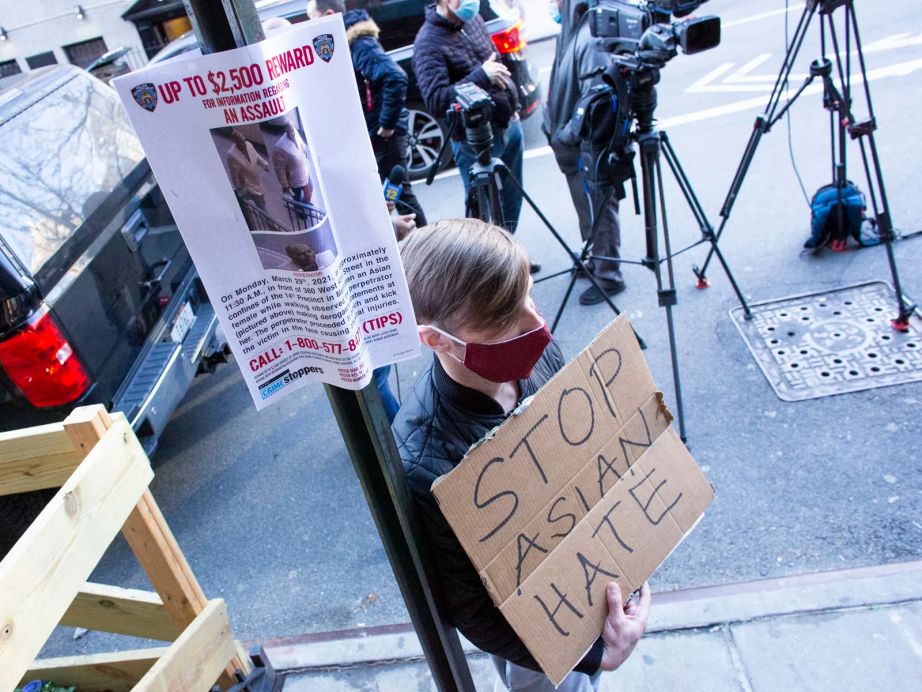 A man holds a sign after an Asian American anti-violence press conference Tuesday outside the building where a 65-year-old Asian woman was attacked in New York City.