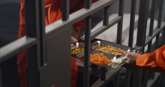 A prison officer serving food to an inmate through the bars of a cell.