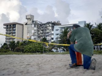 A man kneels in front of the collapsed Champlain Towers South condominium, which shows significant damage, as rescue efforts continue in Surfside, Florida.