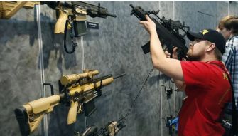 A person examines a display of various assault rifles at an exhibition.