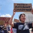 A person holding a sign reading "Protect Birthright Citizenship" during a protest, with others in the background holding various signs related to immigration rights. A person holding a sign reading "Protect Birthright Citizenship" during a protest, with others in the background holding various signs related to immigration rights.