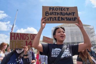 A person holding a sign reading "Protect Birthright Citizenship" during a protest, with others in the background holding various signs related to immigration rights.