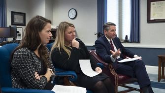 Three individuals seated in a meeting, discussing topics related to disability rights and community-based care services.
