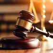 A wooden gavel placed on a sounding block with a blurred background of legal scales and books, symbolizing justice and legal proceedings. A wooden gavel placed on a sounding block with a blurred background of legal scales and books, symbolizing justice and legal proceedings.