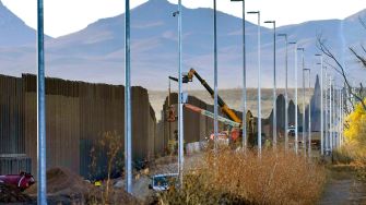 Construction equipment and a partially built section of the border wall between the United States and Mexico, with mountains in the background.