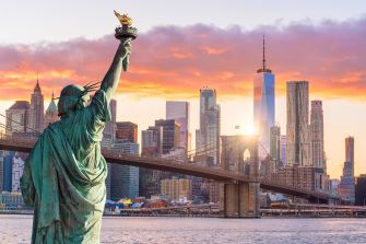 The Statue of Liberty with the New York City skyline in the background during sunset.