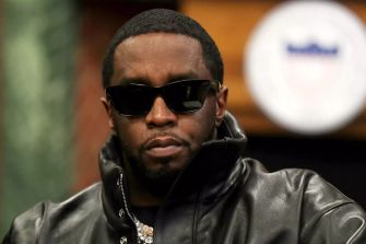 Sean Combs wearing sunglasses and a black leather jacket, seated with a serious expression.