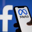 A person holding a smartphone displaying the Meta logo, with the Facebook logo visible in the background. A person holding a smartphone displaying the Meta logo, with the Facebook logo visible in the background.