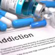 An assortment of drug-related items, including pills, a syringe, and a vial, with the word "Addiction" prominently displayed on a document. An assortment of drug-related items, including pills, a syringe, and a vial, with the word "Addiction" prominently displayed on a document.