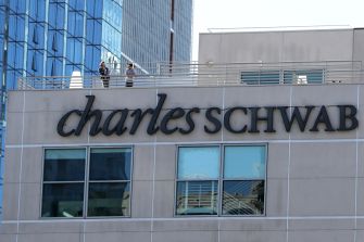 Signage of Charles Schwab building with two people on the rooftop.