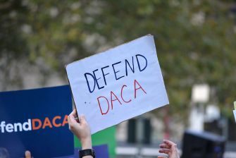 A person holding a sign that reads "DEFEND DACA" at a protest supporting the Deferred Action for Childhood Arrivals program.
