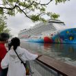 Two people watch a large cruise ship docked at a port. Two people watch a large cruise ship docked at a port.