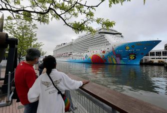Two people watch a large cruise ship docked at a port.