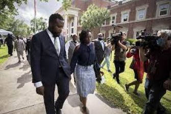 A man and a woman walking together surrounded by media cameras outside a courthouse.