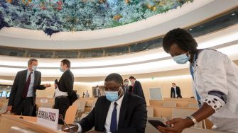 A meeting setting in a United Nations conference room, with delegates wearing masks, engaged in discussion.