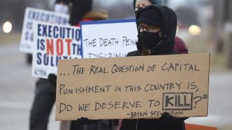 A person holding a protest sign questioning the morality of capital punishment, surrounded by others holding similar signs.
