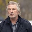 Alec Baldwin walking outside with a serious expression, wearing a black jacket over a plaid shirt. Alec Baldwin walking outside with a serious expression, wearing a black jacket over a plaid shirt.
