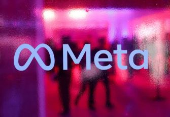 Logo of Meta with blurred figures in the background, illuminated by purple and pink lights.