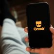 Image of a smartphone displaying the Grindr logo while a person in casual clothing holds it, with their legs visible in the background. Image of a smartphone displaying the Grindr logo while a person in casual clothing holds it, with their legs visible in the background.