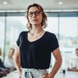 A confident female lawyer standing in a modern office setting, with colleagues engaged in discussion in the background. A confident female lawyer standing in a modern office setting, with colleagues engaged in discussion in the background.