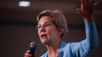 A woman speaking into a microphone while gesturing, with a focus on student loan issues.