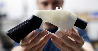 A person holding a partially assembled 3D-printed gun in a workspace.