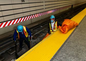Two workers in safety gear performing maintenance on subway tracks.