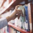 A person reaching for a book on a library shelf. A person reaching for a book on a library shelf.