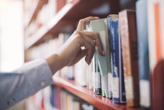 A person reaching for a book on a library shelf.