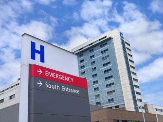 Hospital building with a sign indicating the emergency entrance and south entrance under a blue sky with clouds.