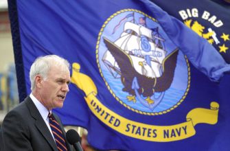 A man speaking at a podium in front of a United States Navy flag.