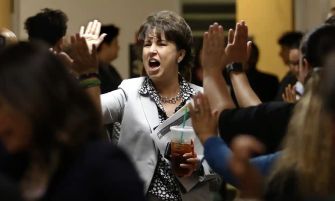 A woman passionately advocating in a crowd, holding a beverage and greeting supporters.
