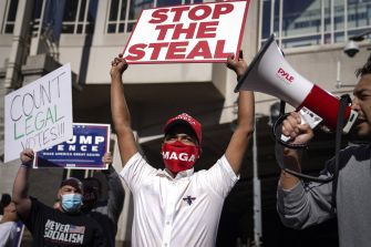 A group of people protesting with signs, including one that says "STOP THE STEAL" and another that says "COUNT LEGAL VOTES!!!"