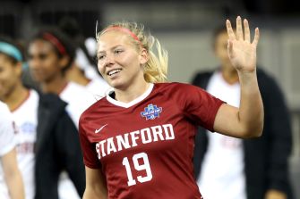 A Stanford University soccer player waving during a match, wearing a red jersey with "Stanford" and the number 19.