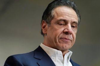 Former Governor Andrew Cuomo looking down, appearing contemplative, during a press event.